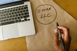 Close-up of hand writing 'Form LLC' on craft paper beside a laptop, indicating business planning.